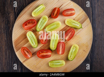 Fresca tagliata poco mature cetrioli e pomodori ciliegia su un tagliere di legno. Vista dall'alto. Stile rustico. Foto Stock