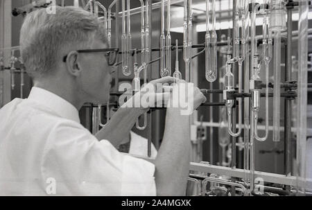 Anni sessanta, storico, un maschio di studente universitario lavora con una serie di provette in vetro fissato su un telaio metallico in un laboratorio di scienze, STATI UNITI D'AMERICA. Foto Stock
