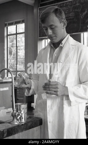 Anni '60, storico studente maschile indossando un camice bianco e miscelando i fluidi in un laboratorio chimico presso l'Università della California del Sud, USA. Foto Stock