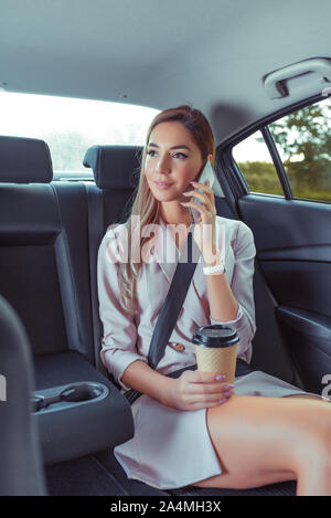 Business Woman in auto taxi, rosa per la concia della pelle tuta, squilla sul telefono cellulare, incontro con gli amici, noleggio auto car sharing. Rigorosa valutazione lady business, cup Foto Stock