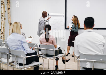 Due diversi colleghi che hanno discusso i concetti di business durante una lavagna a fogli mobili la presentazione in un ufficio sala seminario Foto Stock