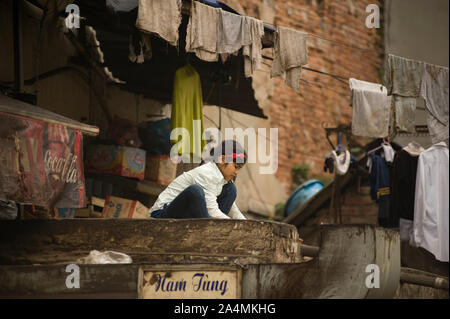 La città di Ho Chi Minh (Saigon), Vietnam - Marzo 02, 2011: giovane ragazza vietnamita pulisce i vestiti per la famiglia negozio di generi alimentari si trova sotto la terrazza di sporco Foto Stock