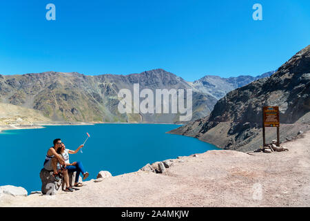Il Cile, montagne delle Ande. Coppia giovane prendendo un selfie con un bastone selfie presso il Embalse el Yeso (El Yeso Dam), montagne delle Ande, Cile, Sud America