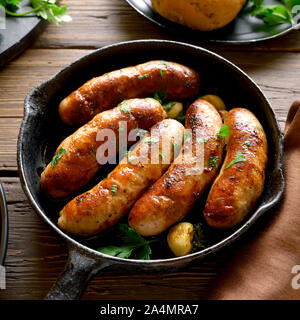 Salsicce arrostite in padella su sfondo di legno. Foto Stock