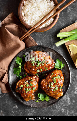 Grigliata di cosce di pollo e una ciotola di riso su pietra scura sullo sfondo. Gustosi piatti in stile asiatico. Vista superiore, laici piatta Foto Stock