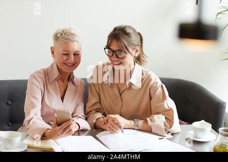 Coppia imprenditrice mostrando qualcosa al suo collega il telefono mobile e sorridente durante il loro lavoro di squadra in ufficio Foto Stock