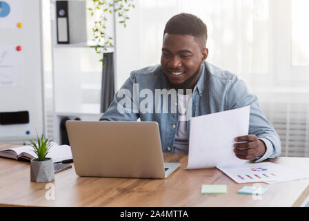 Giovane imprenditore nero a lavorare con il computer portatile e i documenti di office Foto Stock