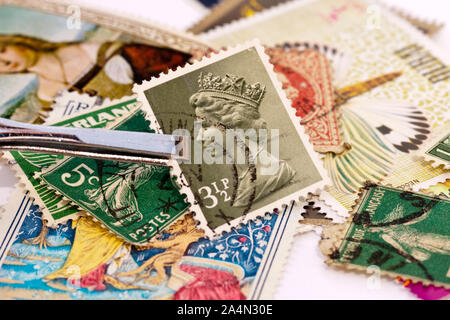 Pinzette a molla tenendo un Regno Unito francobollo con Queen Elizabeth 2 lato verticale. Collezioni di francobolli in background. Foto Stock