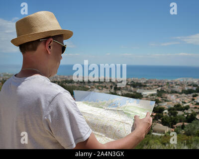 Giovane maschio turistico con una mappa dell'area ritiene la città sulla costa, closeup, vista posteriore Foto Stock