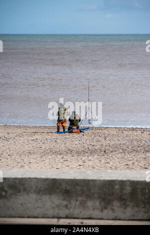 Due uomini in camouflage riveste la pesca in mare con aste in riva al mare in Hornsea East Yorkshire su una soleggiata giornata autunnale Foto Stock