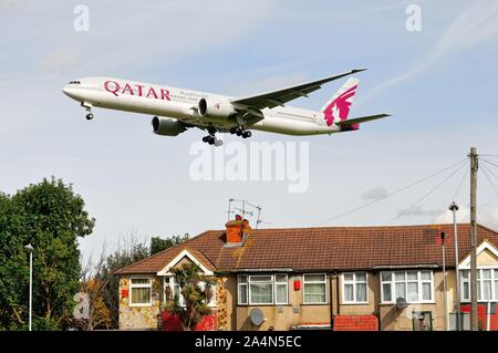 La Qatar Airways Boeing 777-300 jet volando a bassa quota sopra i tetti a Hatton Cross sul suo approccio di atterraggio a Heathrow Londra Inghilterra REGNO UNITO Foto Stock