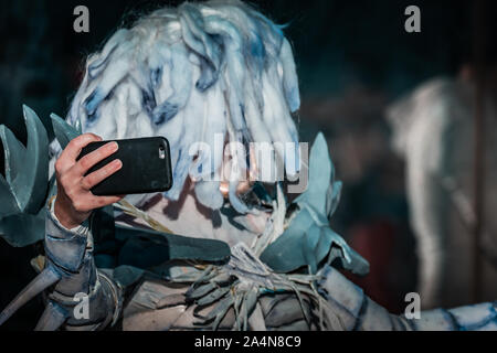 Selfie Zombie. Bianco morto nevoso regina costume, cosplayer ragazza con uno smartphone verso di sé. La luce naturale del giorno, ora d'oro di ripresa macro. Foto Stock
