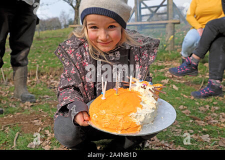 Bambina di 6 anni mentre tiene il suo ginger orange cat torta di compleanno che celebra la sua festa di compleanno all'aperto al di fuori del Galles UK KATHY DEWITT Foto Stock