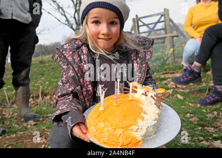 Bambina di 6 anni mentre tiene il suo ginger orange cat torta di compleanno che celebra la sua festa di compleanno all'aperto al di fuori del Galles UK KATHY DEWITT Foto Stock