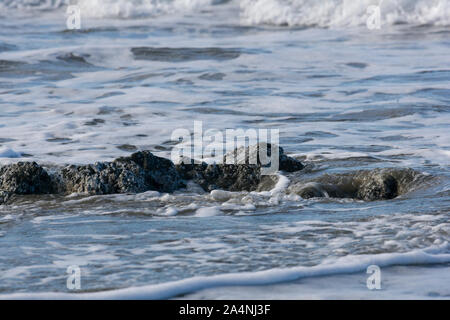 Onde che lambiscono intorno rocce sulla spiaggia Foto Stock