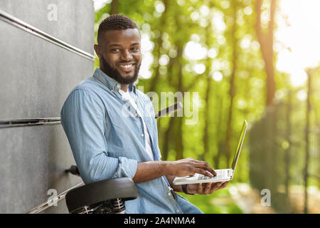 Nero sorridente freelancer laptop di contenimento esterno e appoggiata sulla bicicletta Foto Stock