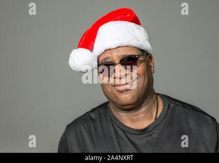 Sorridente African American uomo che indossa un rosso e bianco Santa Claus hat contro uno sfondo a tinta unita Foto Stock