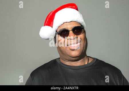 Pippo African American uomo con la sua linguetta sporgente, indossando un rosso e bianco Santa Claus hat contro uno sfondo a tinta unita Foto Stock