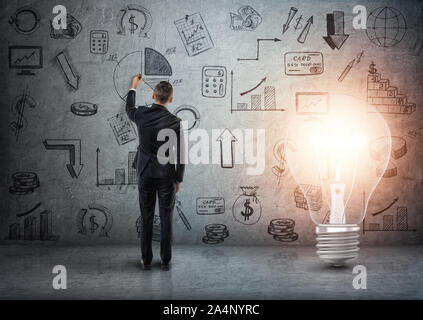 Vista posteriore di un imprenditore di disegno scarabocchi business sulla parete di cemento con grande luce incandescente lampadina accanto a lui Foto Stock