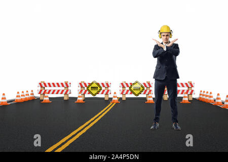 Imprenditore nel casco giallo e le cuffie in piedi sulla strada in costruzione con le braccia incrociate in gesto di arresto Foto Stock