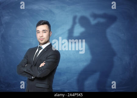 Imprenditore in piedi su sfondo blu con un'ombra con le mani sul capo dietro di lui