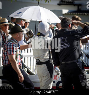 Driver e meccanica in attesa nel calore dell'azienda paddock con un ombrello per ombra al 2019 Goodwood, Sussex, Regno Unito. Foto Stock