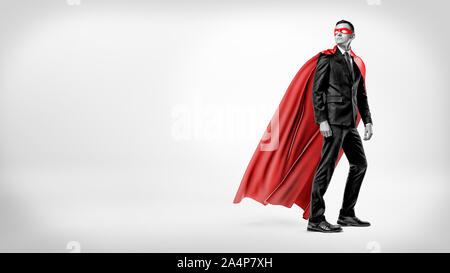 Un imprenditore in un fluire red superhero cape e una maschera guardando sopra la sua spalla su sfondo bianco. Foto Stock