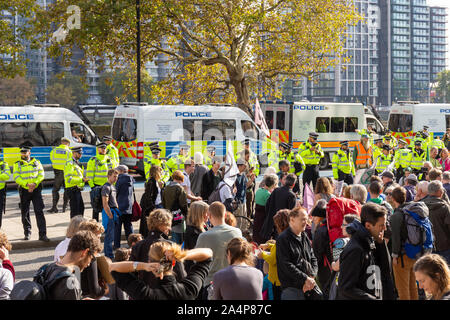 Millbank, London, Regno Unito 15 ottobre 2019; estinzione della ribellione manifestanti con una linea di funzionari di polizia dietro. Fila di furgoni di polizia in background Foto Stock