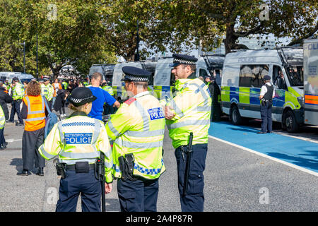 Millbank, London, Regno Unito 15 ottobre 2019; vista posteriore di tre funzionari di polizia in corrispondenza di una ribellione di estinzione protestare con una fila di furgoni di polizia in background Foto Stock