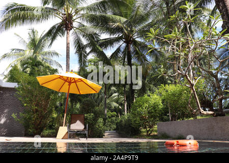 Piscina e lettini con ombrellone sotto le palme da cocco. Resort tropicale, il concetto di relax e di vacanza Foto Stock