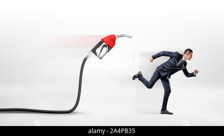 Un imprenditore su sfondo bianco di scappare da un gas di colore rosso ugello attaccata ad un tubo flessibile nero. Foto Stock