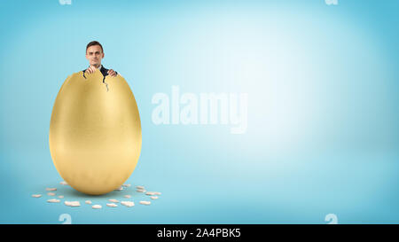 Un happy businessman guarda dall'interno di un gigante Golden Egg con la rottura di una parte superiore. Foto Stock