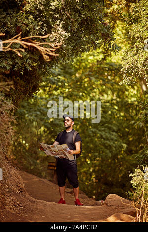 Adulto caucasica escursionista guardando intorno tenendo premuto Controllo mappa stradale. Uomo bello nella foresta. Backpacker escursionismo trascorrere vacanze Foto Stock