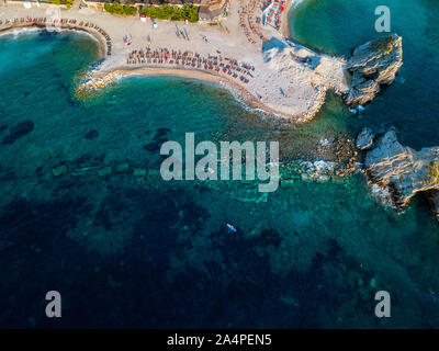 Vista aerea di Sveti Nikola, isola di Budva, Montenegro. Hawaii spiaggia, ombrelloni e bagnanti e acque cristalline. Coste frastagliate Foto Stock