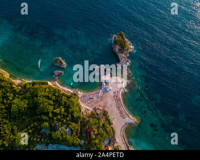 Vista aerea di Sveti Nikola, isola di Budva, Montenegro. Hawaii spiaggia, ombrelloni e bagnanti e acque cristalline. Coste frastagliate Foto Stock