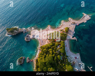 Vista aerea di Sveti Nikola, isola di Budva, Montenegro. Hawaii spiaggia, ombrelloni e bagnanti e acque cristalline. Coste frastagliate Foto Stock