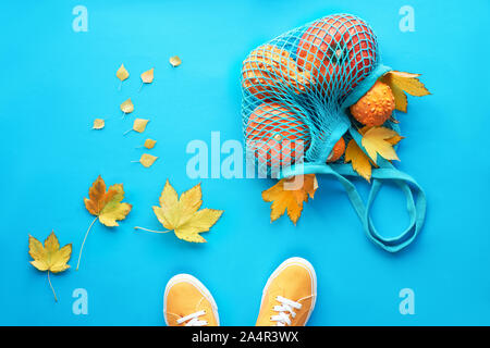 Autunno laici piatta su fondo azzurro. Zucche arancione in borsa a rete o borsa a rete, giallo foglie di acero e coppia di scarpe di tela. Foto Stock