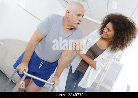 Accompagnatore senior aiuta l uomo a piedi con il telaio Foto Stock