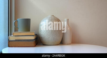 La minima area di lavoro con vasi di ceramica sul tavolo bianco con libri e caffè verde cup Foto Stock