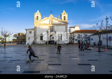 Ragazzi giocare e pattinaggio di fronte la chiesa di Santa Maria. Lagos, Algarve, Portogallo, Aprile 2019 Foto Stock