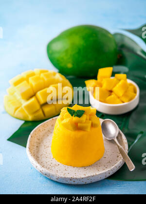 Mousse di mango su sfondo blu con copia spazio a sinistra. Giallo deliziosa mousse di mango con fette di mango maturo. Verticale. Foto Stock