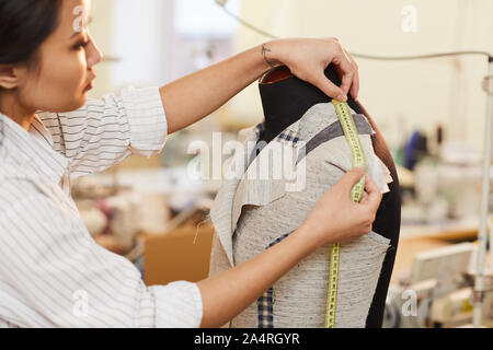 Sarta asiatici prendendo le misure da giacca sul manichino durante la fase di cucitura in officina Foto Stock