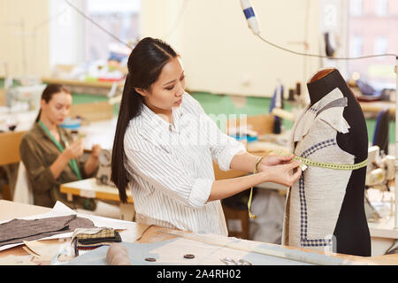 Femmina asiatica sarto camicia di misurazione sul manichino con misura di nastro durante la fase di cucitura per il cliente Foto Stock