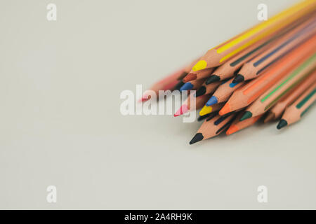 Più matite di diversi colori per disegnare, impilati su uno sfondo bianco, appaiono dalla parte superiore destra di uno sfondo bianco Foto Stock