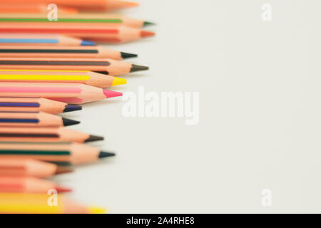 Appuntite matite colorate che compaiono a partire dal lato sinistro della carta di sfondo che è bianco, allineati in profondità. Foto Stock