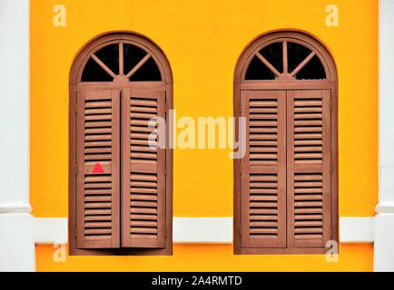 Coppia di finestre ad arco con mobili di antiquariato in legno marrone scuri su giallo esterno del negozio tradizionale casa in Bugis Junction, Singapore Foto Stock