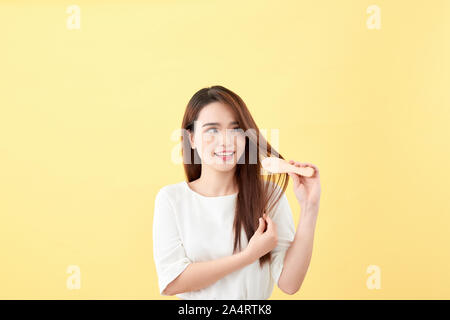 Ritratto di attraente donna sorridente spazzolare i capelli isolato su giallo studio shot Foto Stock