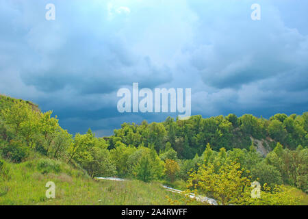 Paesaggio con thundercloud su verde foresta. Storm cloud verde sopra vegetazioni. Bella raincloud su con blu scuro nuvole. La natura prima di pioggia. Foto Stock