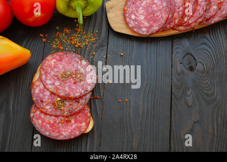 In casa il fast food. Fare sandwich. Affettati e verdura matura giacciono su legno scuro tavolo. Per la preparazione di sandwich con salsiccia. Sul buio Foto Stock