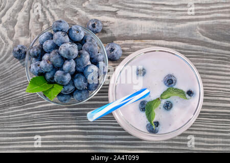 Frullato di frutti di bosco o yogurt in vetro e mirtilli nella ciotola sul tavolo di legno Foto Stock